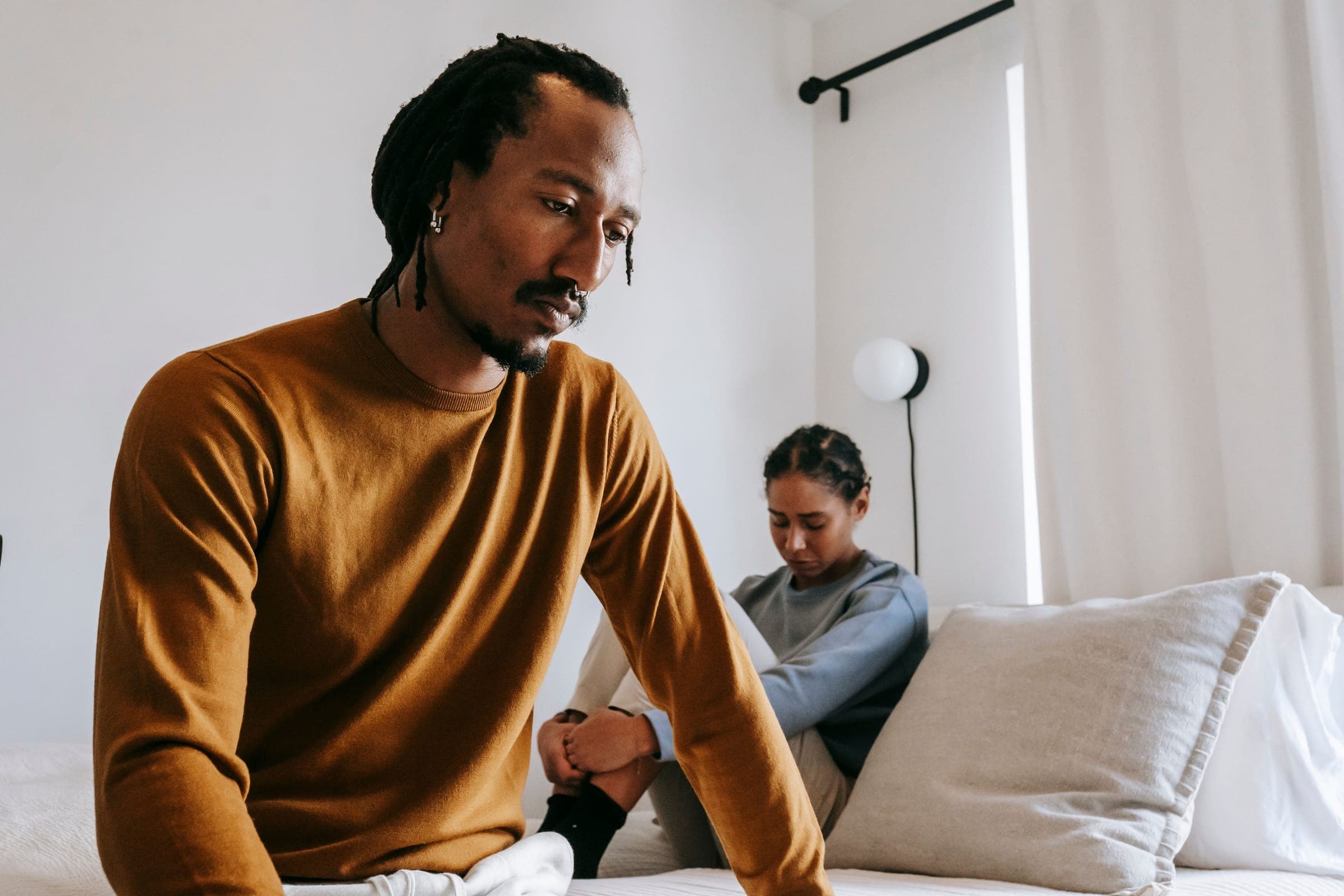 A couple in deep thought and conflict sitting apart in a bedroom