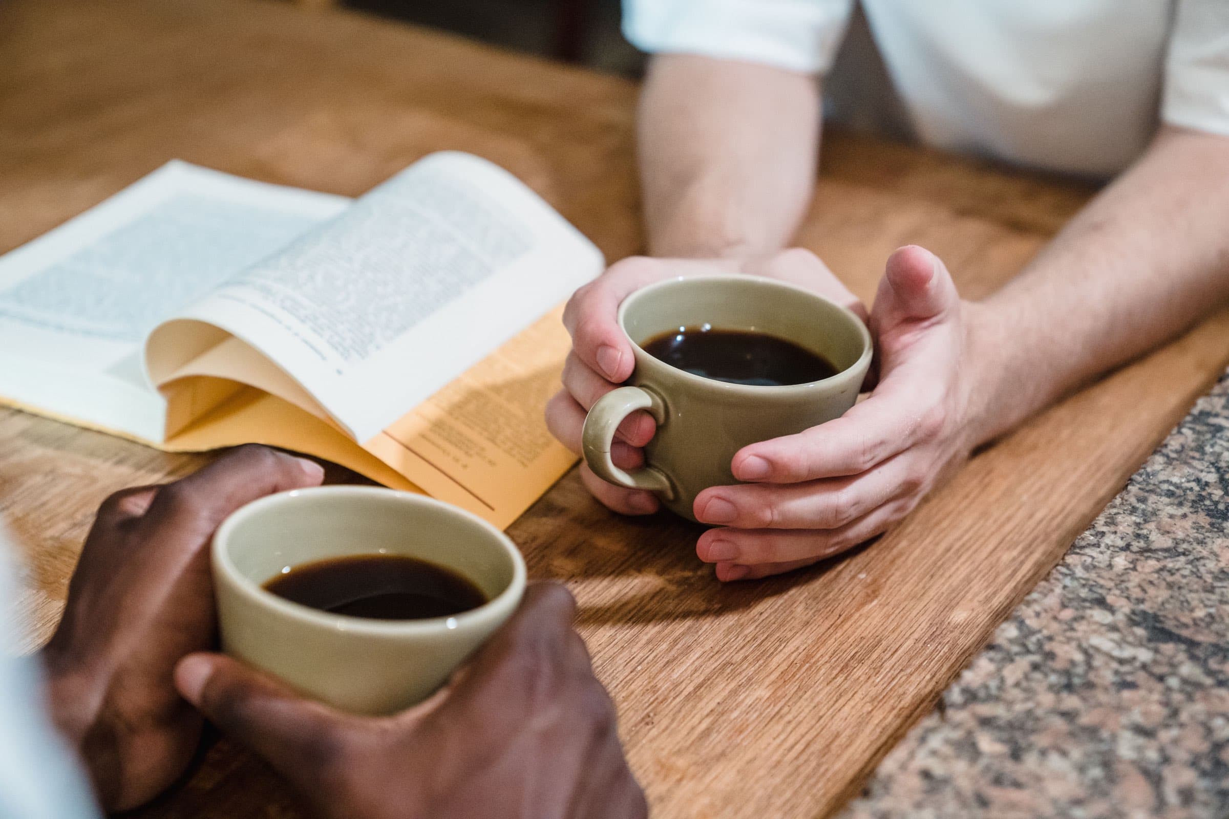 Two people sharing coffee across a wooden table beside an open book