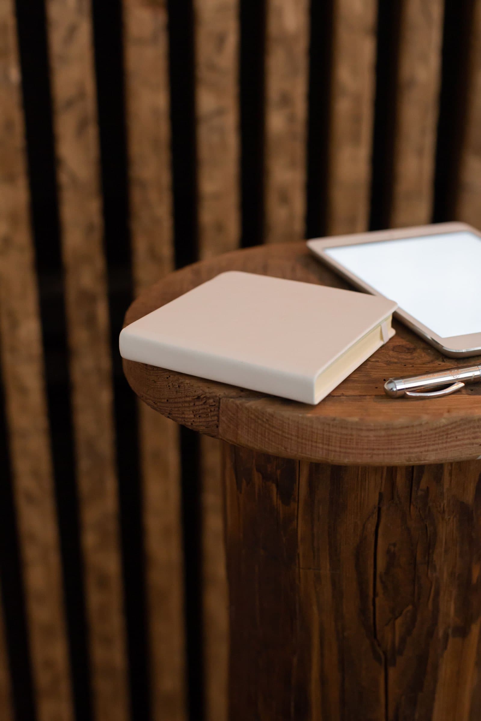 A notebook, pen and tablet on a round wooden side table