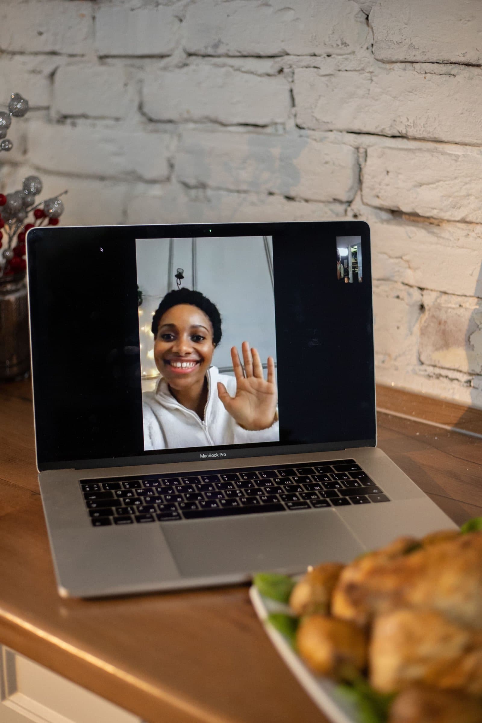 A smiling woman waving on a video call on a laptop at a kitchen counter